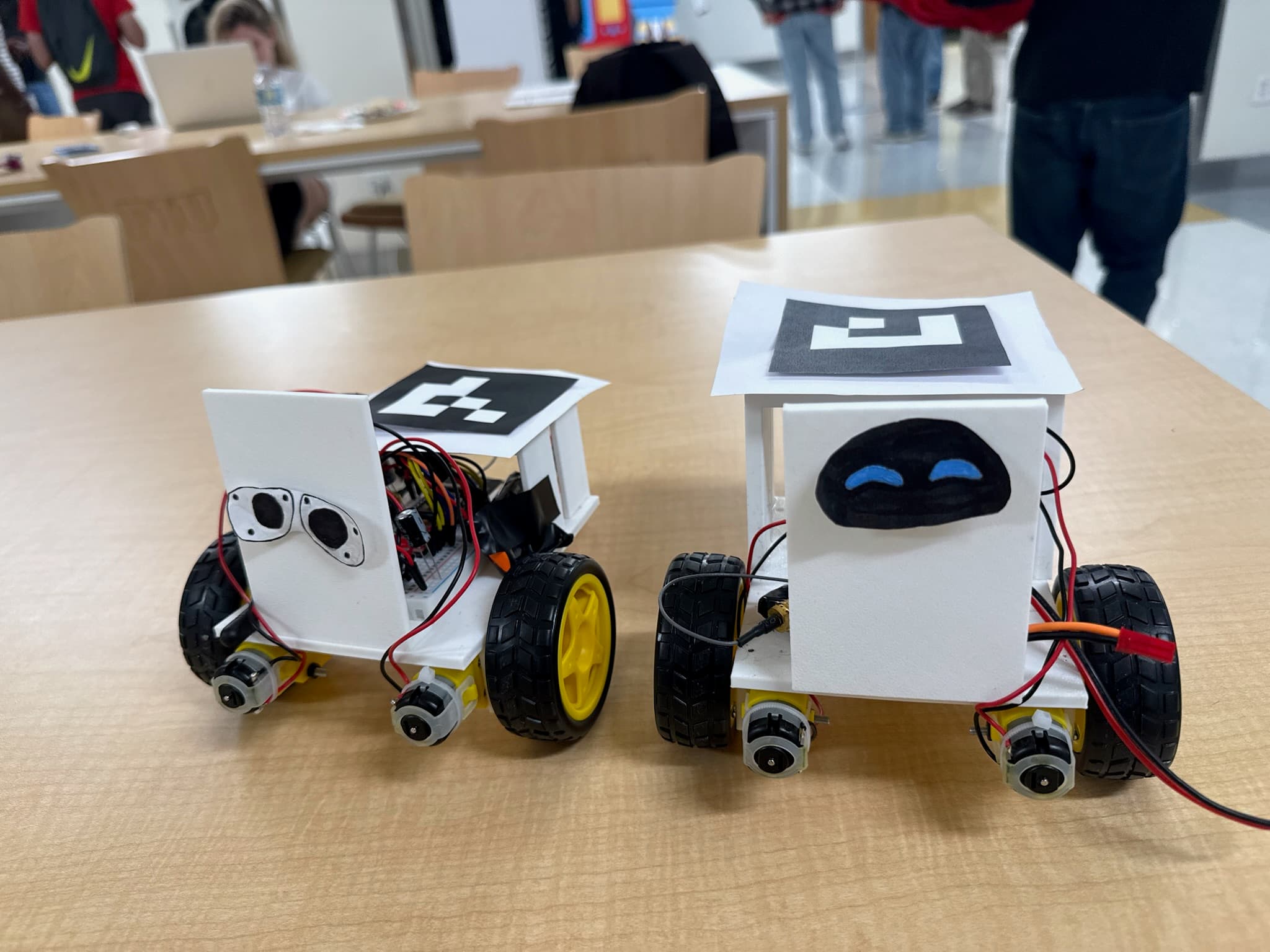 Two wheeled robots with hand-drawn faces, exposed electronics, and visual markers on top.