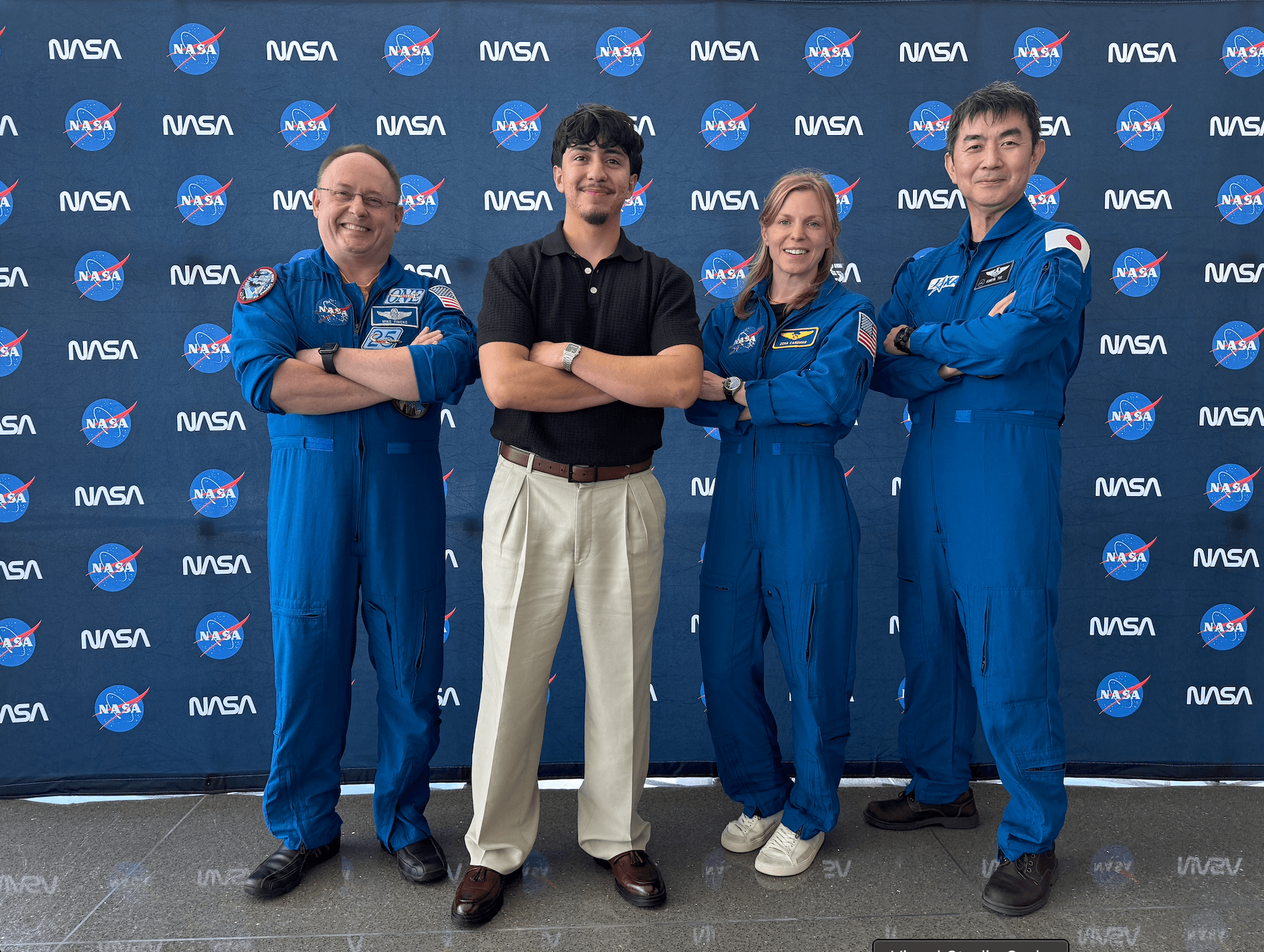 Pablo posing with three people in blue flight suits in front of a NASA backdrop.